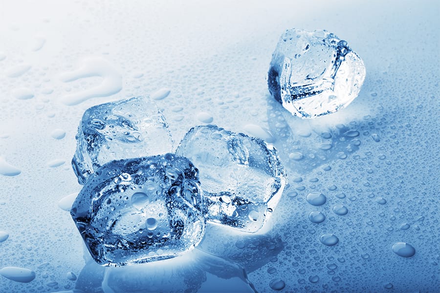 A close up shot of ice cubes on a blue surface. They are partially melted.