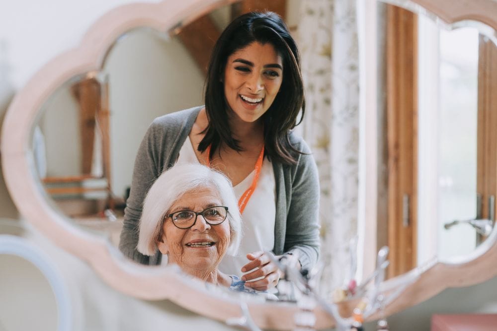 live-in-carousel-1000x667 Two ladies stand in front of a mirror. An elderly lady sits smiling, a younger lady stands behind her smiling. The younger lady wears an orange lanyard.