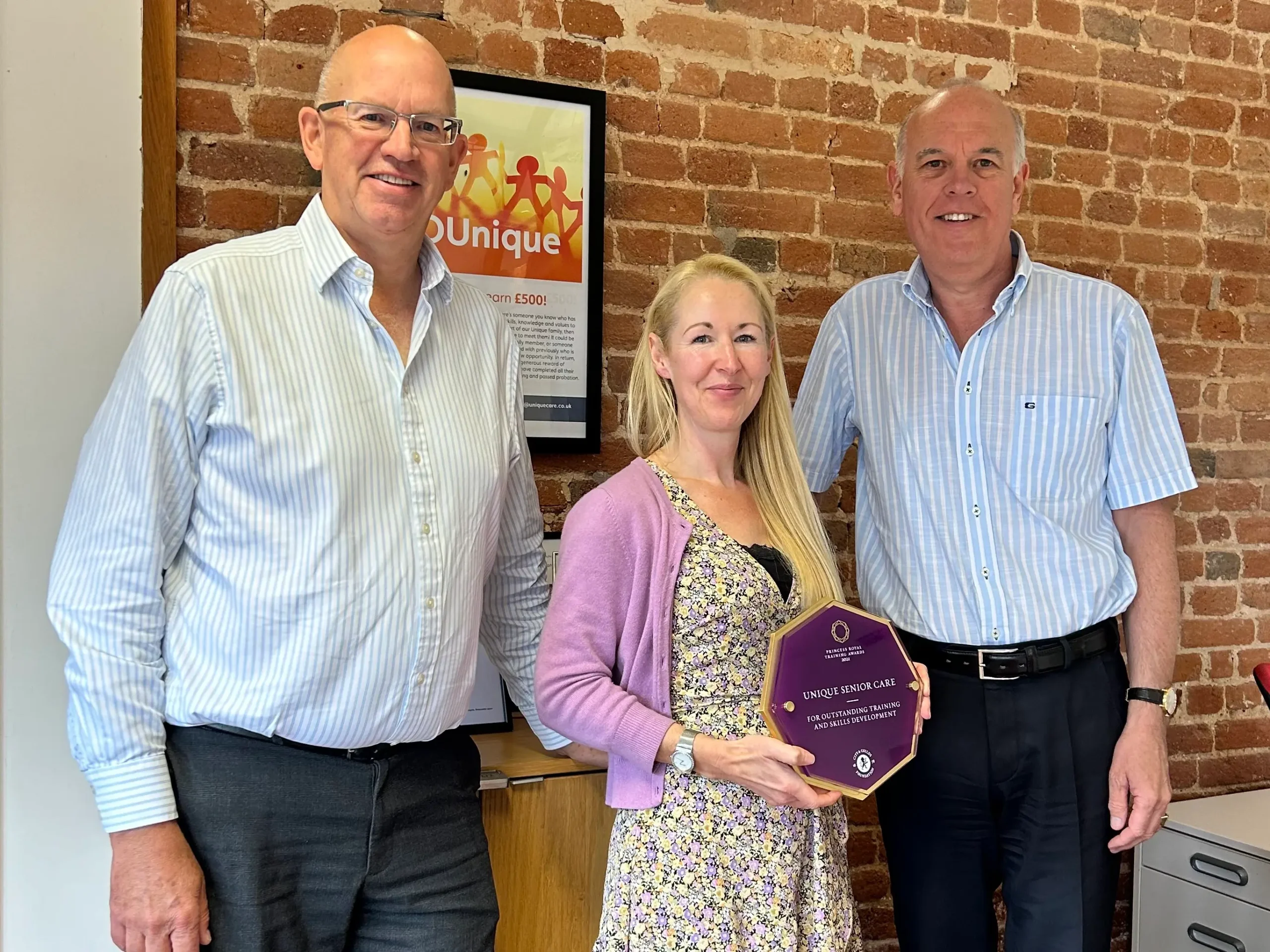 Phil Maundrill, Director, Jo Cleary, Learning and Development Manager, and Phil Wright-Howarth, Director, standing together, smiling and holding their Princess Royal Training Award from 2021.