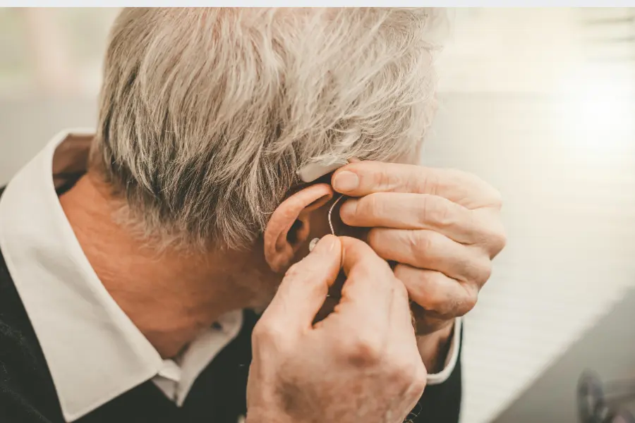 An older man adjusting his hearing aid behind his ear.