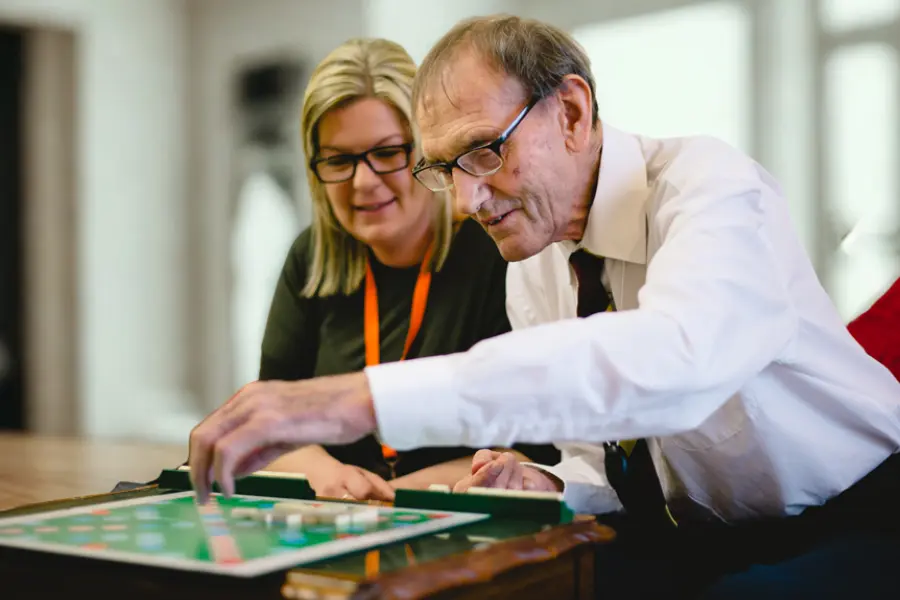 An elderly gentleman and his caregiver playing a board game together