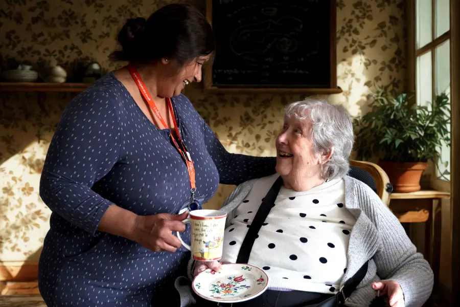 A caregiver and client smiling at eachother while holding a mug and plate