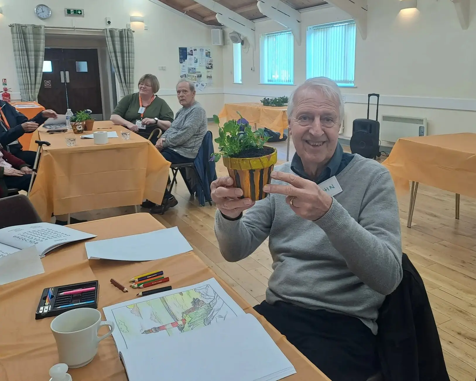 An attendee at the leamington spa and kenilworth memory cafe holding a plant to show the camera while smiling
