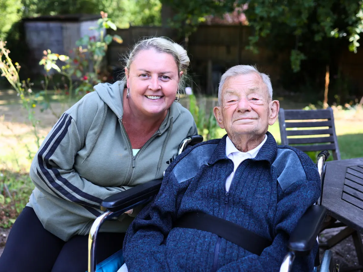 Live-in client, Michael sat next to his caregiver, Angie, in the garden. Both are smiling at the camera