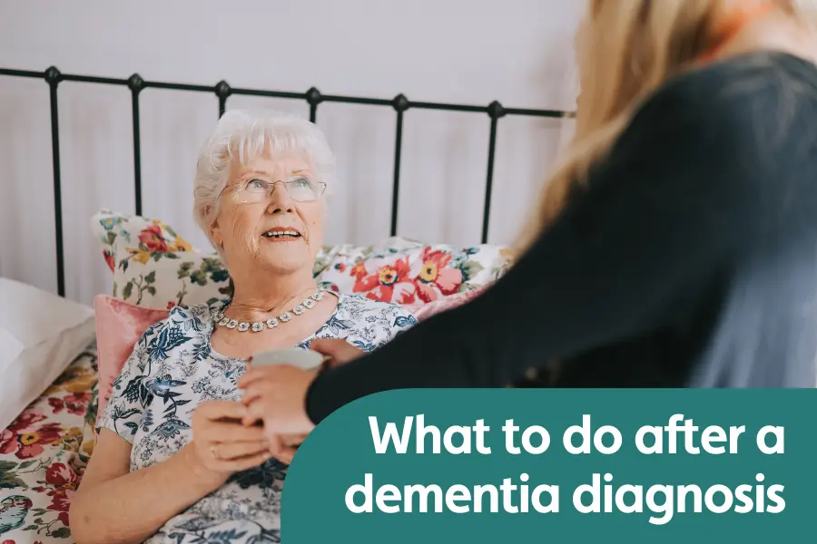 Featured image for blog around what to do after a dementia diagnosis. Image shows an older lady sat in bed smiling at her caregiver while being handed a cup of tea