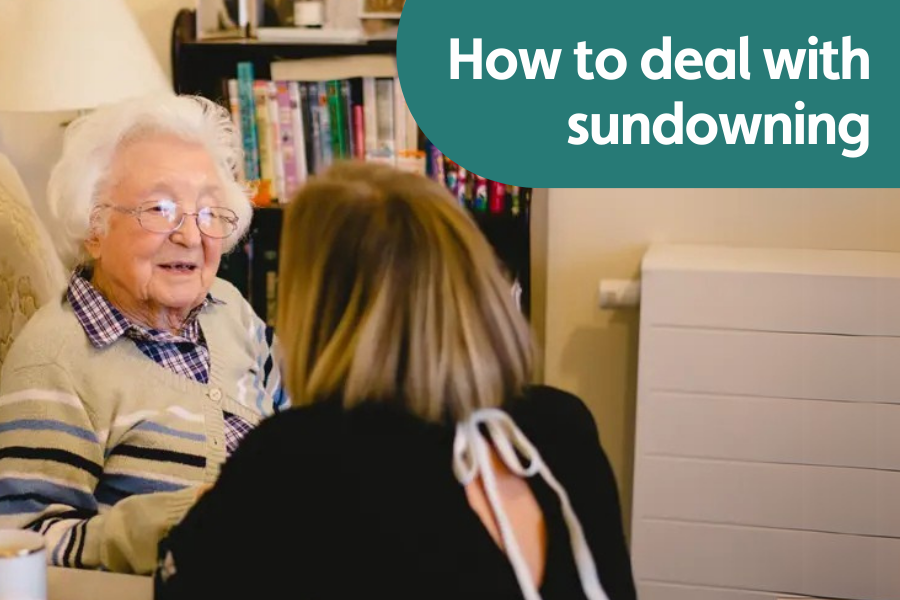 Featured image for blog on how to deal with sundowning. Image shows older lady sat in a chair while a younger woman bends down to talk to her.