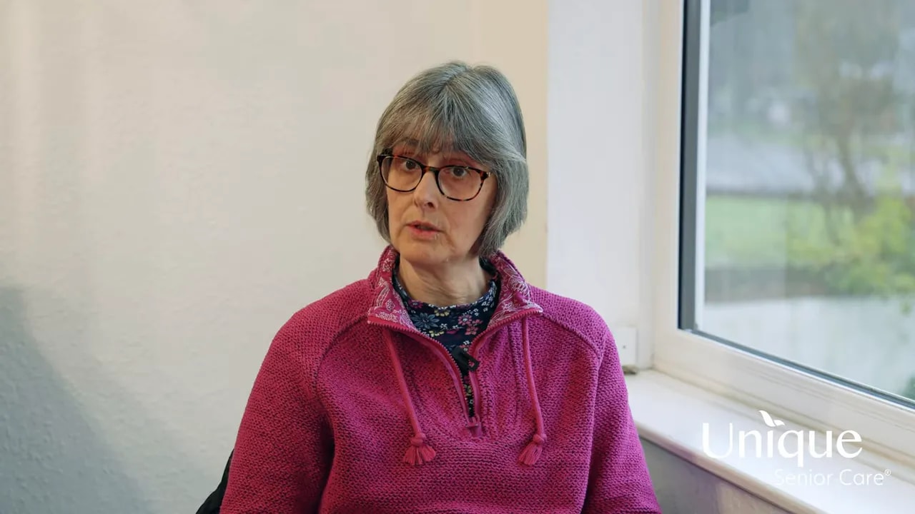 Calm, clear interview of an older woman in a pink jumper by a window conveying reassurance