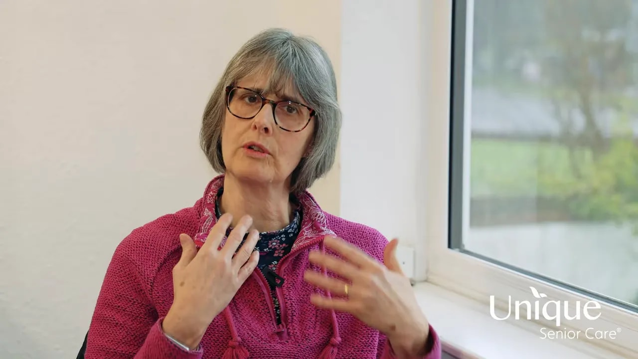 older woman using hand gestures while discussing home care, seated by a window