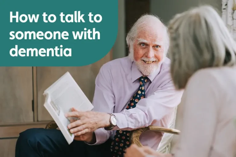 Featured image for blog on how to talk to someone with dementia. Image shows an elderly gentleman showing a woman something in a book while smiling