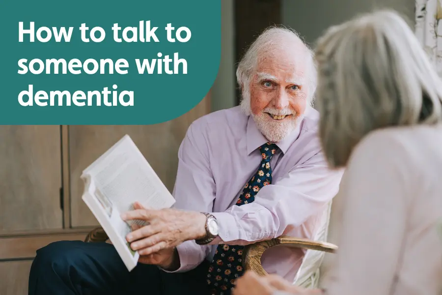 Featured image for blog on how to talk to someone with dementia. Image shows an elderly gentleman showing a woman something in a book while smiling
