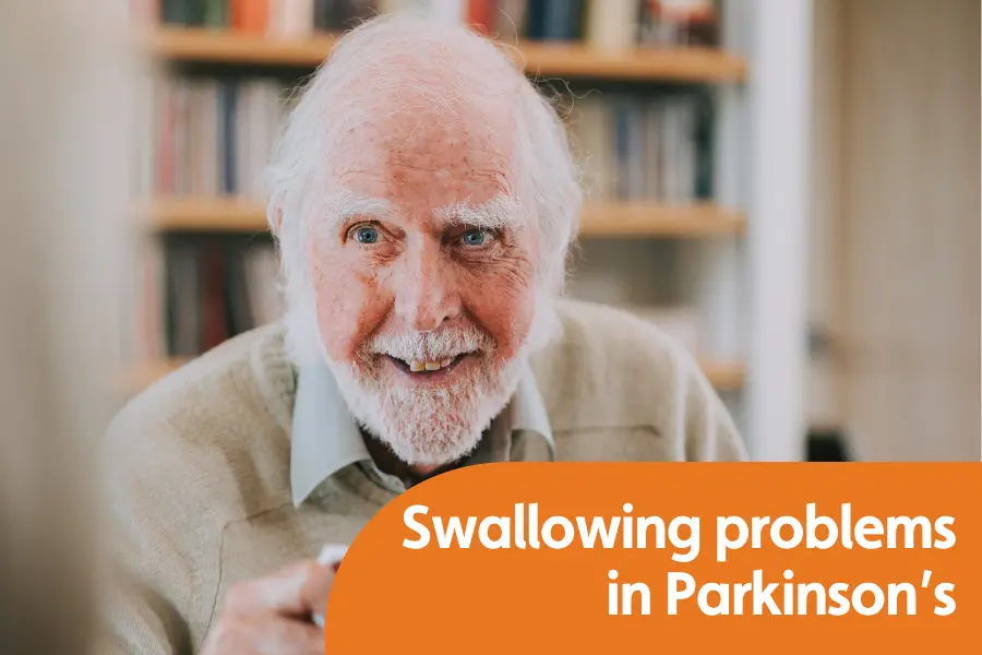 An elderly man smiles to someone off camera while holding a cup of tea. Txt overlay reads 'swallowing problems in Parkinson's'