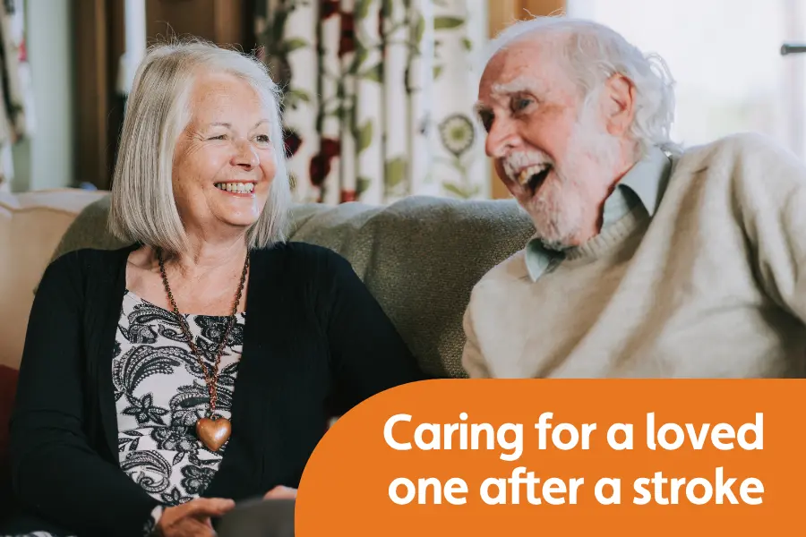 An elderly gentleman and carer sat together smiling during conversation on a sofa. Overlayed text reads 'Caring for a loved one after a stroke'