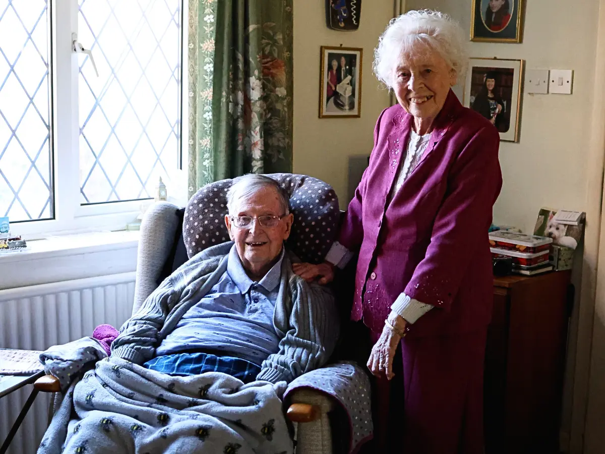 Unique senior clients, Rona and John in their living room at home, smiling towards the camera